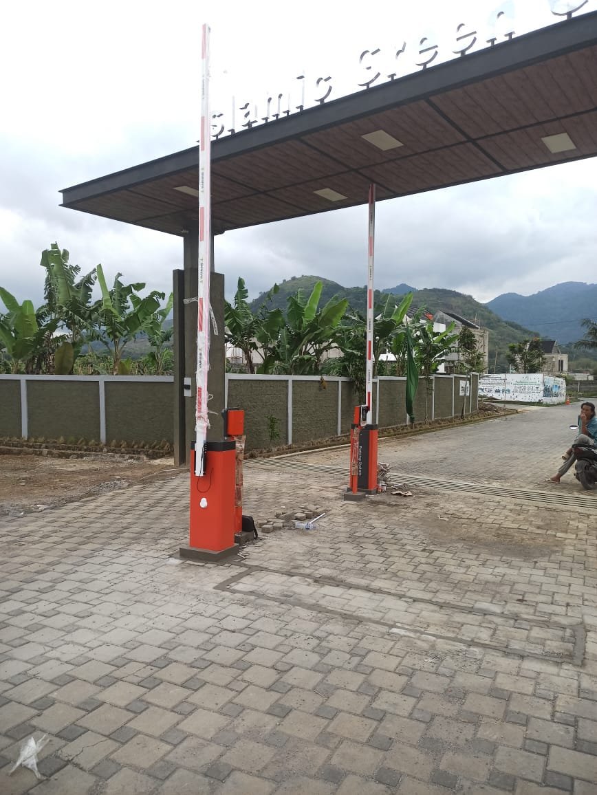 Dua unit palang parkir otomatis (barrier gate) warna oranye hitam untuk akses masuk keluar perumahan dengan sistem kartu RFID yang sedang diinstalasi